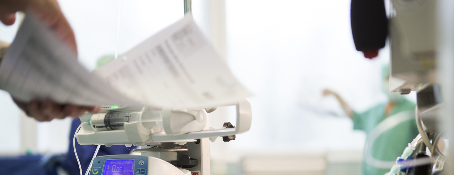 Ein medizinisches Infusionsgerät mit einer Spritzenpumpe wird bedient, während eine Person Patientendokumente überprüft.